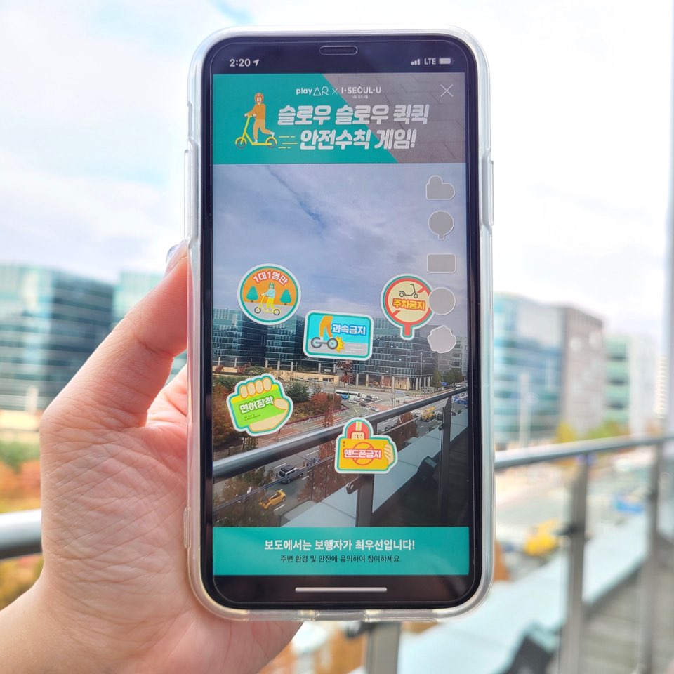 시럽 월렛이 서울시와 함께 진행하는 AR 플랫폼을 활용한 보행도로 안전 캠페인 ‘슬로우 슬로우 퀵퀵 안전수칙 AR게임의 핸드폰 화면이 보이고 있습니다.
